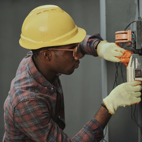 Electrician in a yellow hard hat working on an electrical panel